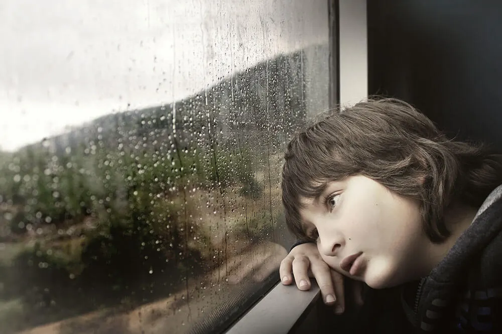 Bambino appoggiato al finestrino di un treno che guarda fuori