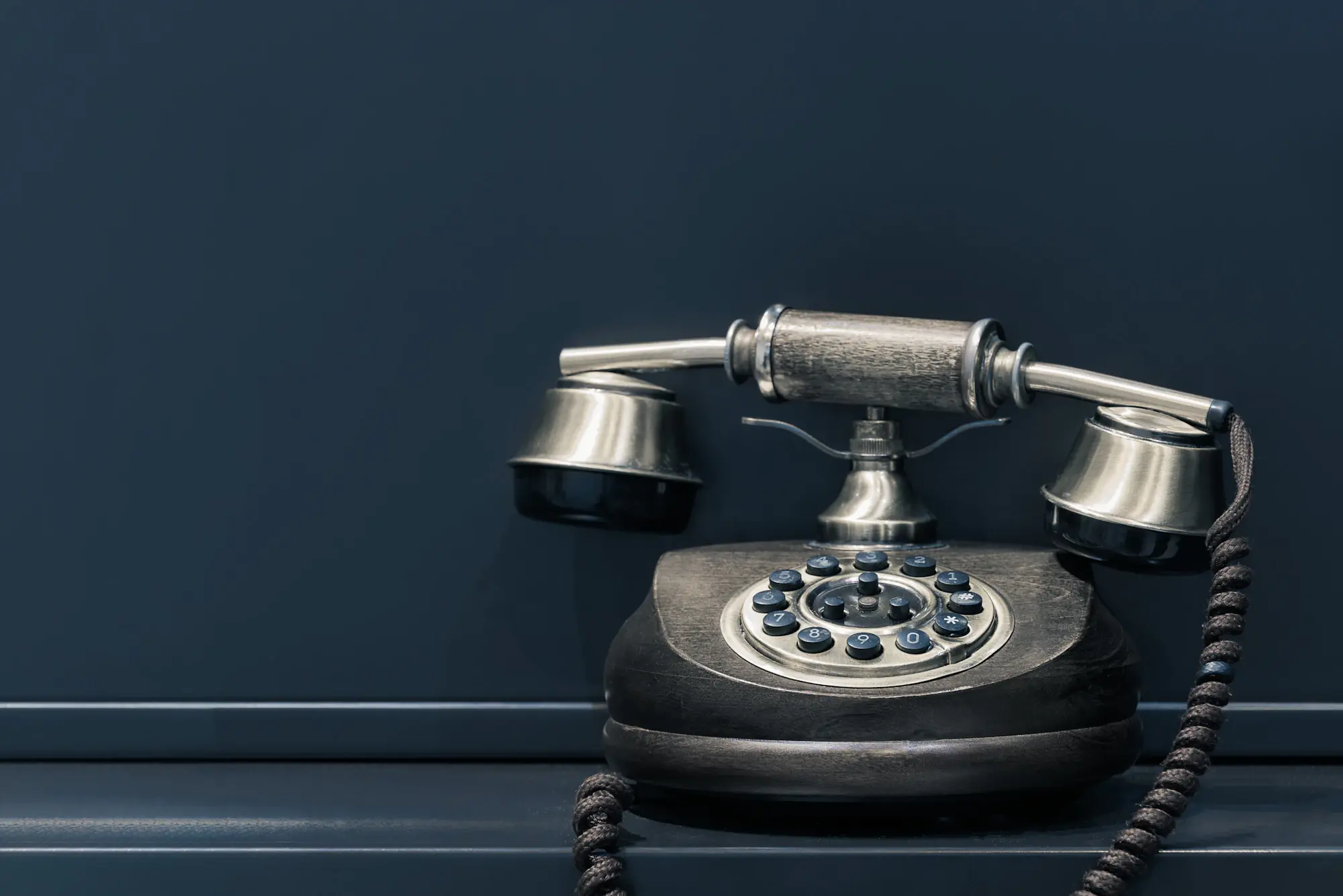 Telefono d'epoca nero e argento appoggiato davanti a una parete blu scuro