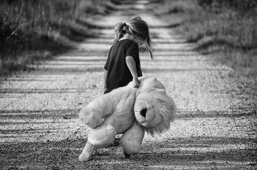 Bambina in bianco e nero che trascina un grande orso di peluche lungo un sentiero
